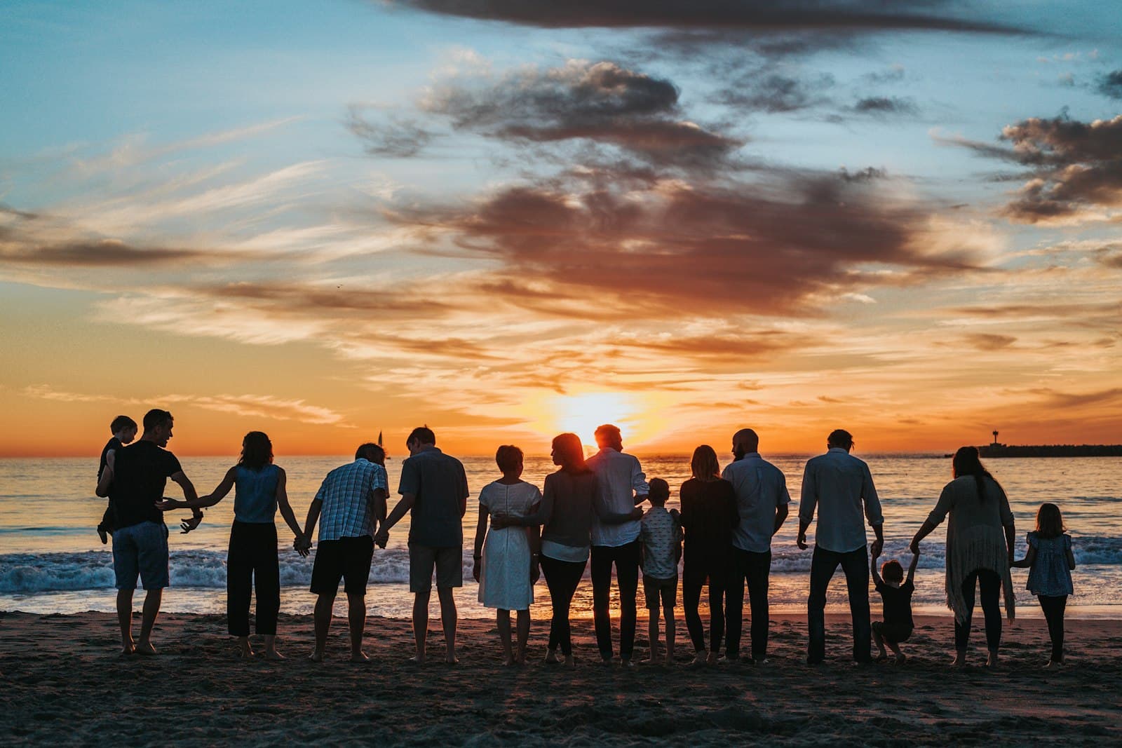 Multi-generational family holding hands on a beach at sunset — connection across generations