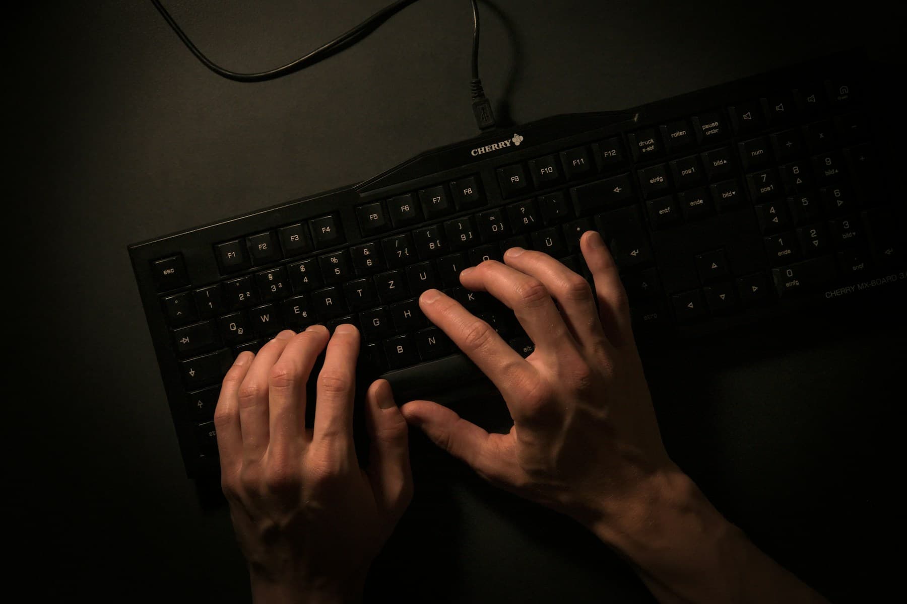 Hands typing on a black keyboard in a dark room, shot from above